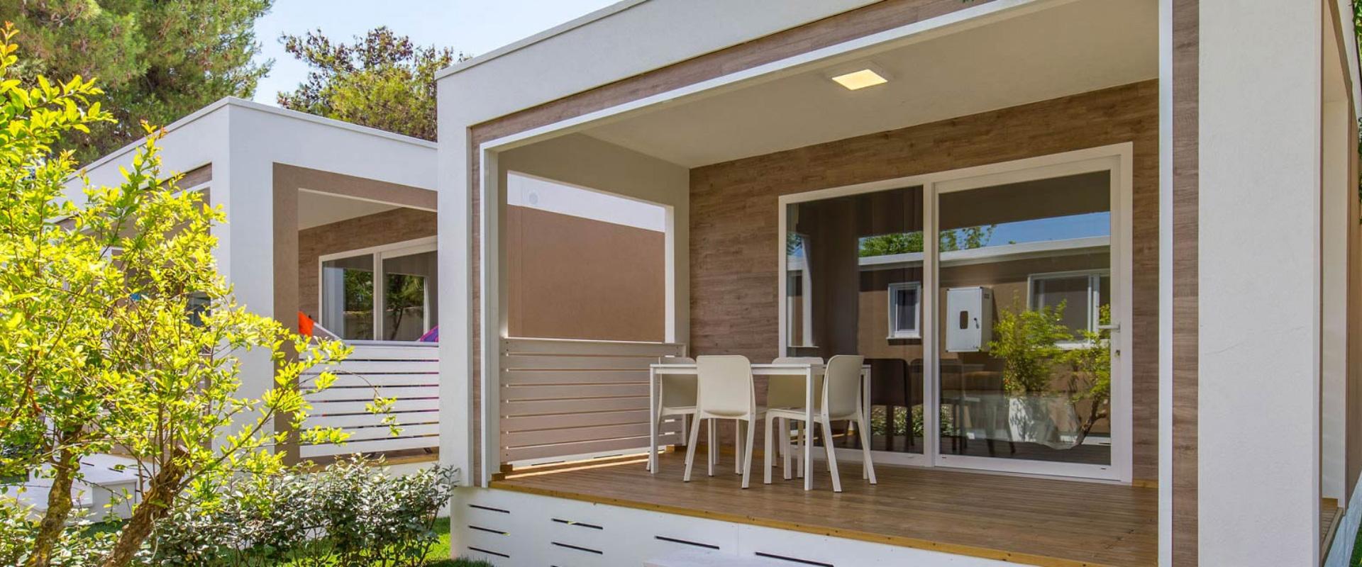 Moderna veranda con tavolo e sedie, circondata da verde e alberi.