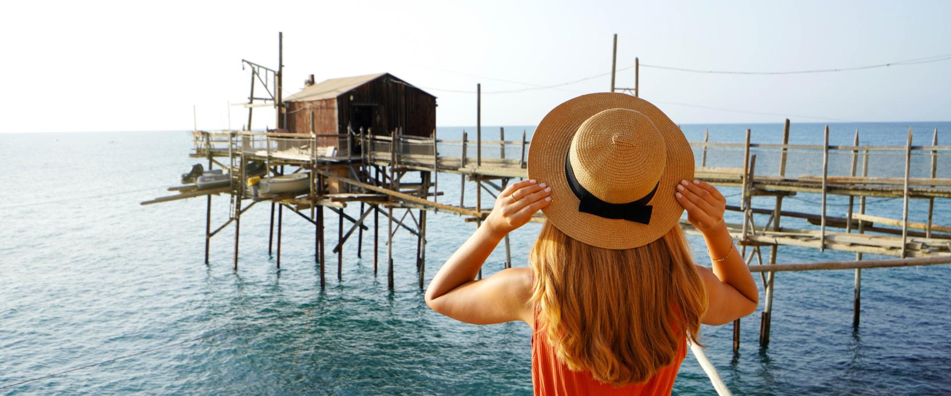 Donna con cappello osserva una palafitta sul mare.