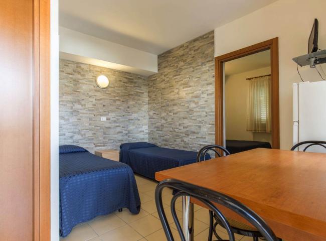 Camera con due letti singoli, tavolo in legno e parete in pietra.