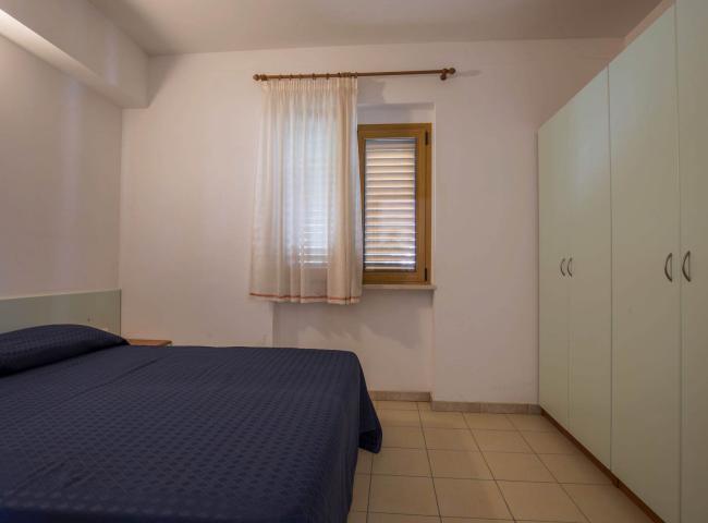 Camera da letto semplice con letto matrimoniale, armadio e finestra con tenda bianca.