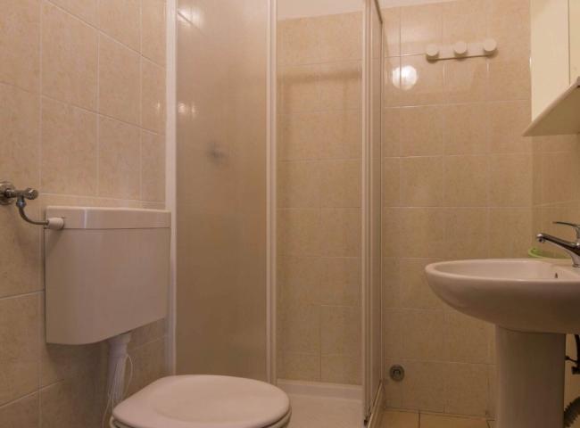 Bagno piccolo con doccia, lavabo e WC, piastrelle beige.
