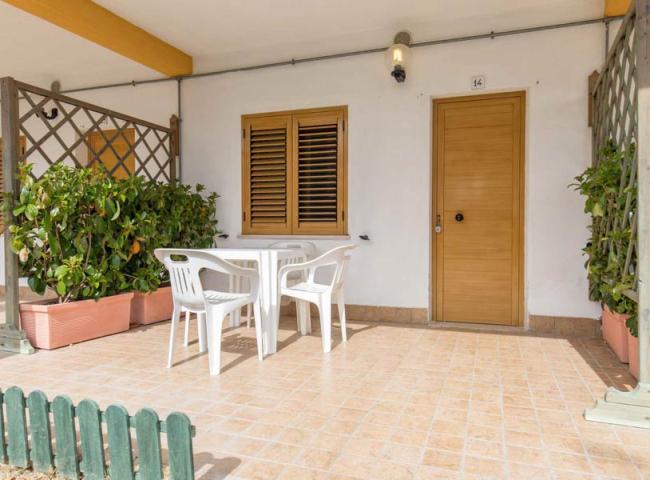 Veranda con tavolo e sedie bianche, piante in vaso, porta e finestre con persiane.