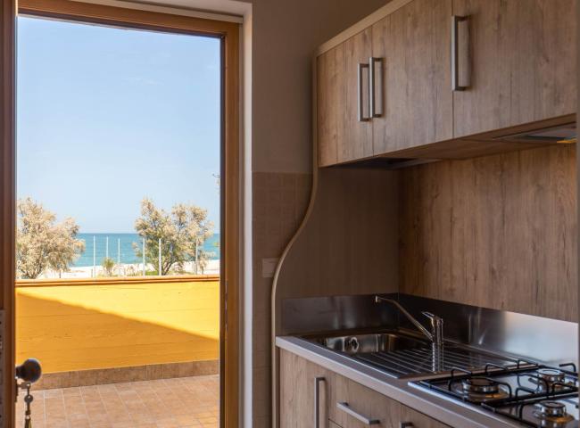 Cucina con vista mare, terrazza e alberi, arredo in legno.