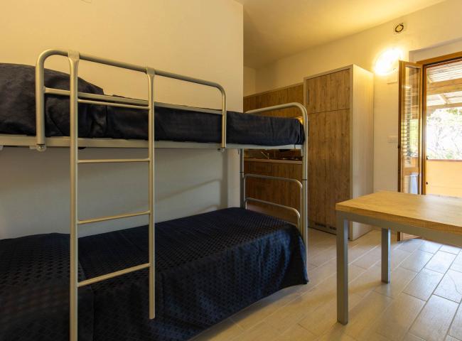 Camera con letto a castello, tavolo in legno e porta finestra aperta.
