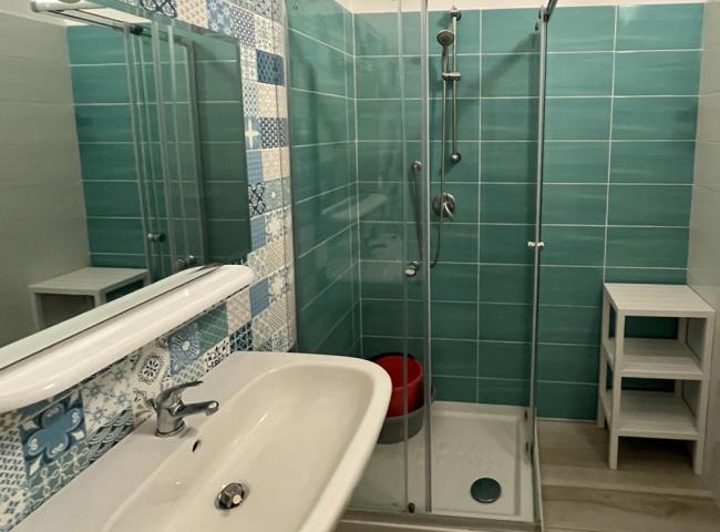 Bagno moderno con doccia, lavabo e piastrelle colorate su parete e pavimento.