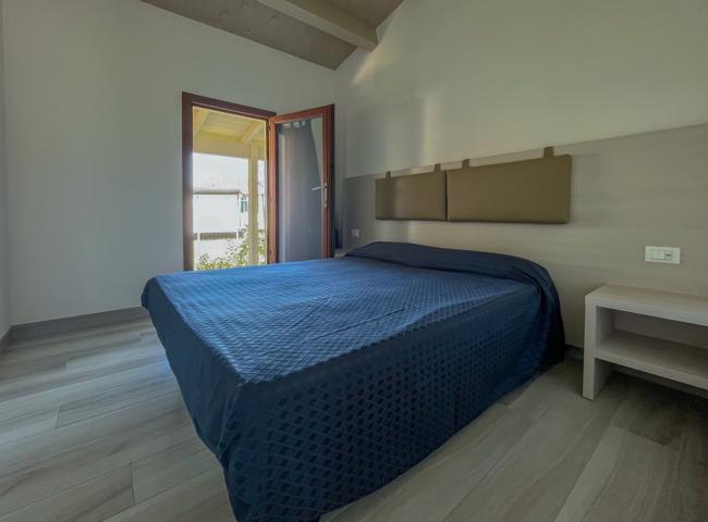 Camera moderna con letto matrimoniale, copriletto blu e accesso al balcone.