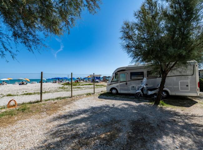 Camper parcheggiato vicino alla spiaggia con ombrelloni colorati e mare sullo sfondo.