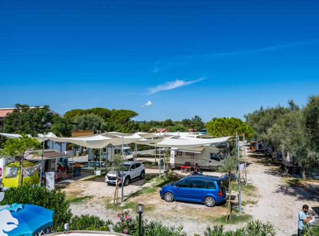 Campeggio con roulotte, auto e tende sotto un cielo azzurro e soleggiato.