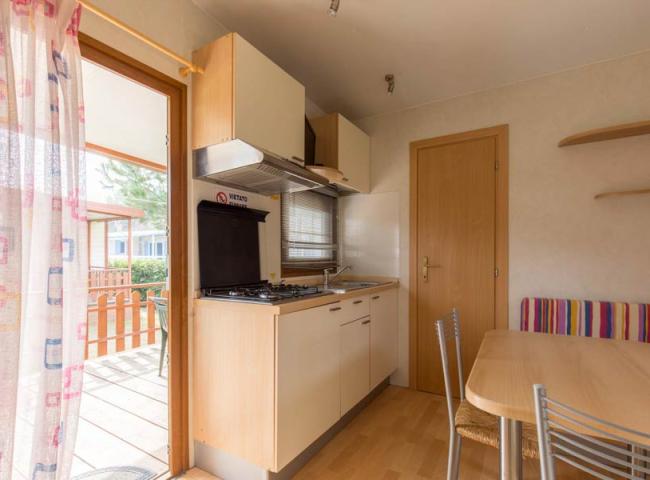 Cucina compatta con fornelli, tavolo, sedie e accesso al patio esterno.