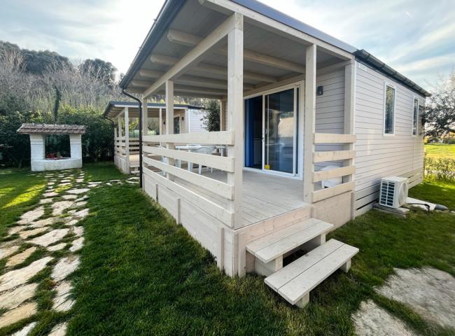 Casetta in legno con veranda, giardino verde e vialetto in pietra.