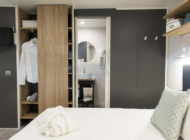 Camera moderna con armadio aperto, bagno in vista e letto ordinato.