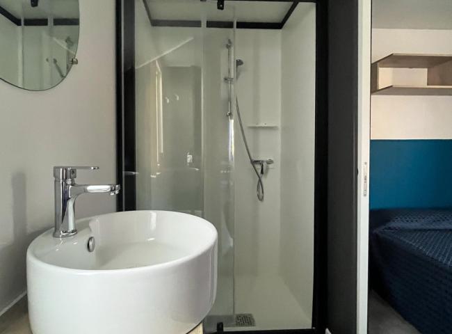 Bagno moderno con lavabo, doccia in vetro e accesso a una camera da letto.