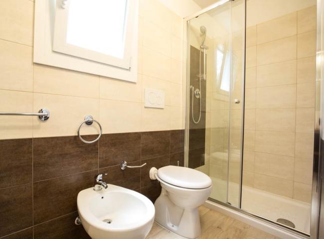 Bagno moderno con doccia, bidet e WC, piastrelle beige e marroni.