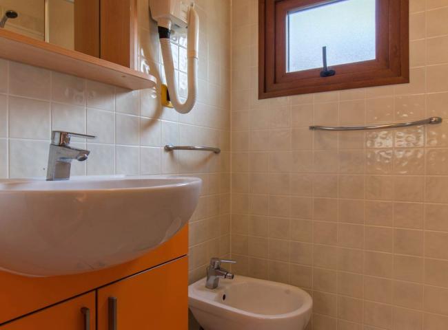 Bagno compatto con lavabo, bidet, finestra e asciugacapelli a parete.