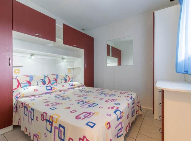 Camera da letto con letto matrimoniale, armadi rossi e copriletto colorato.