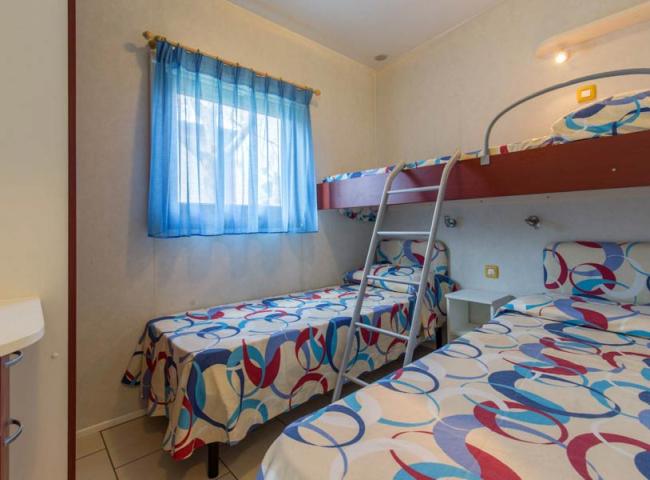 Camera con letto a castello e singolo, arredamento colorato e finestra con tenda blu.