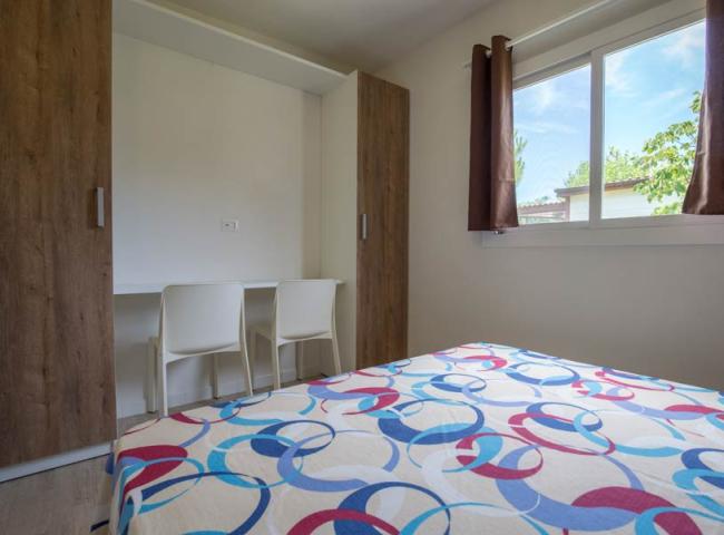 Camera moderna con letto colorato, armadio in legno e finestra luminosa.