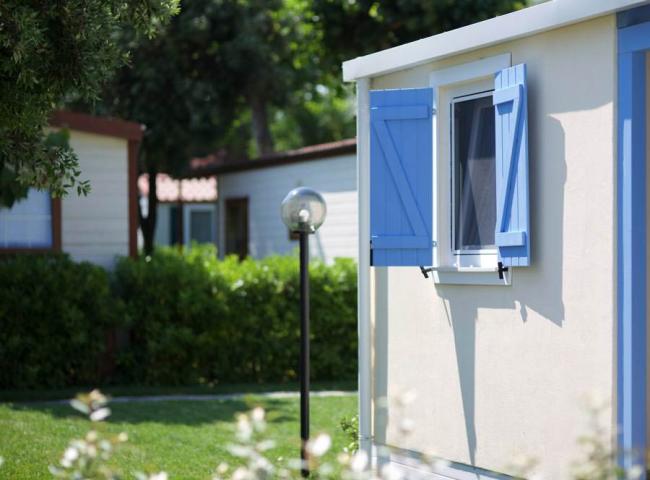Case mobili con finestre azzurre in un ambiente verde e soleggiato.