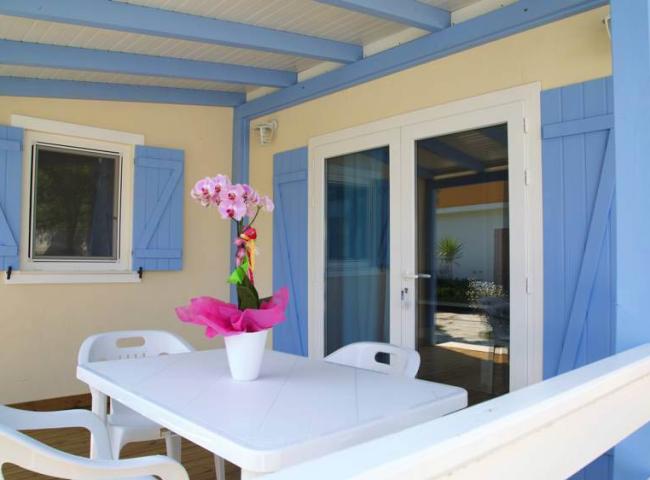 Terrazza con tavolo bianco, sedie e fiori rosa, persiane azzurre.