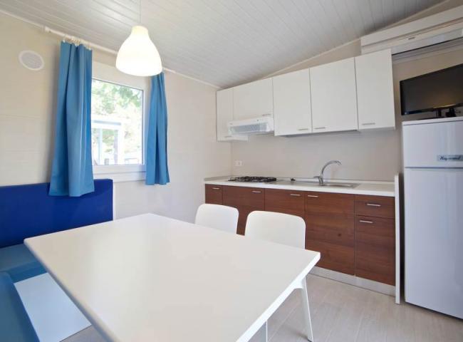 Cucina moderna con tavolo bianco, sedie, e tende blu, frigorifero e mobili in legno.