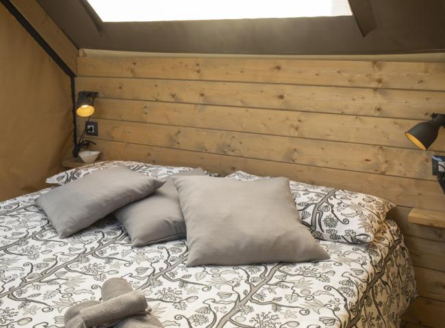 Camera da letto con pareti in legno, cuscini grigi e lampade da lettura.