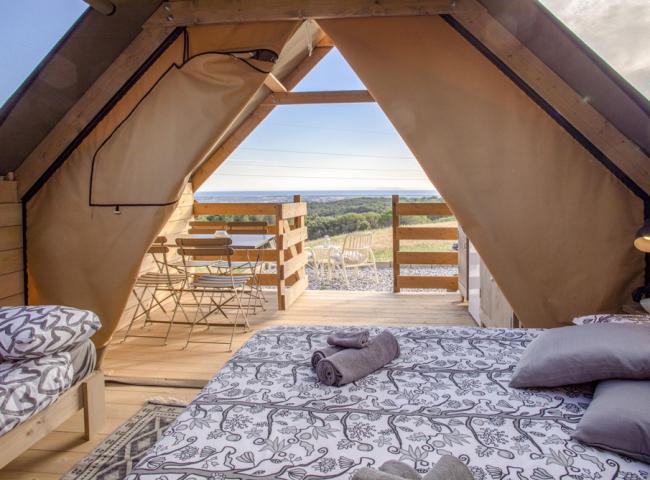 Camera in tenda con vista panoramica, arredi in legno e terrazza esterna.