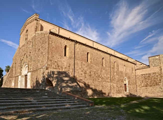 Chiesa medievale in pietra con facciata imponente e cielo azzurro sullo sfondo.